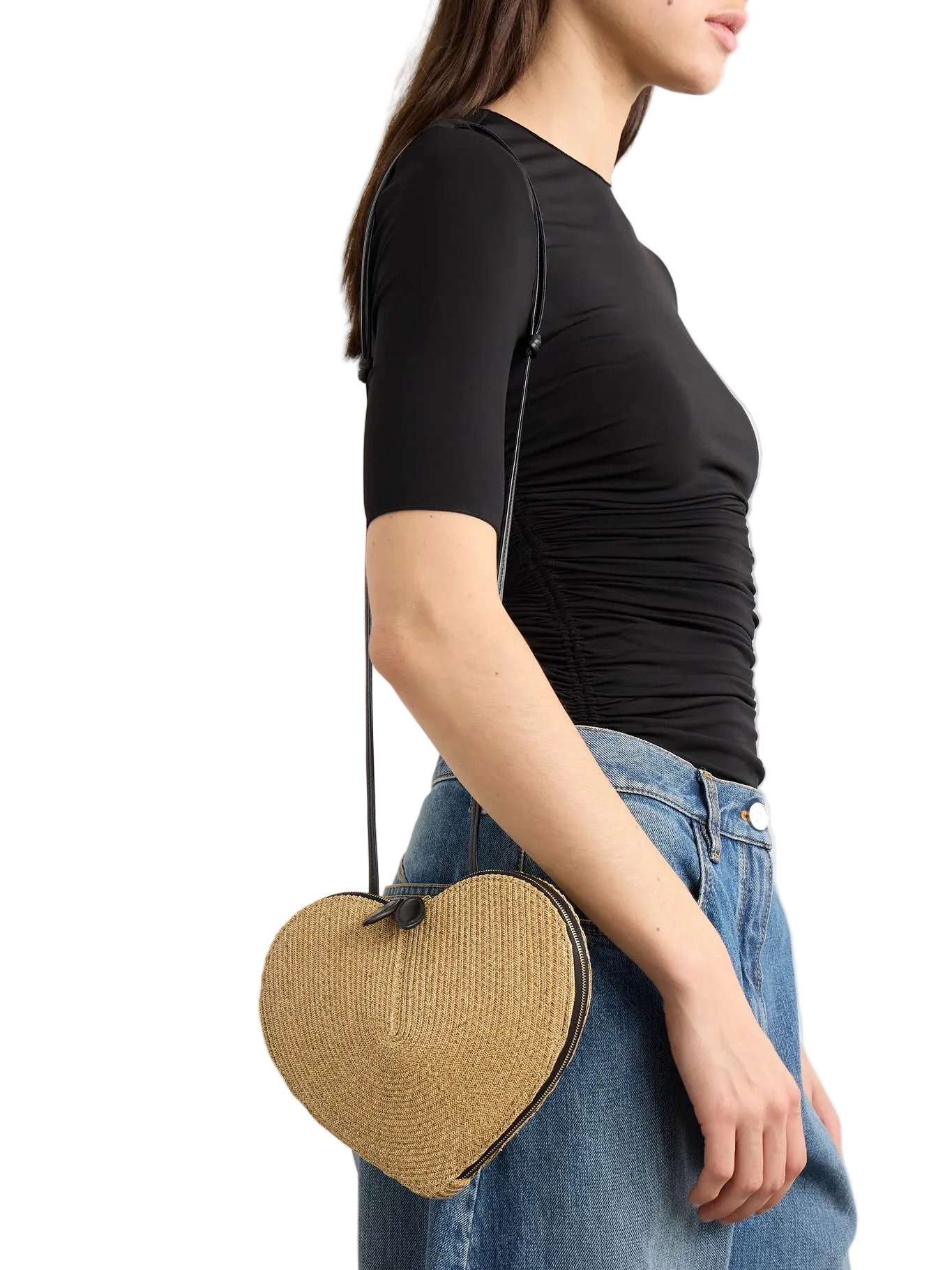 Person wearing a black top and blue jeans with a straw heart-shaped bag on a white background